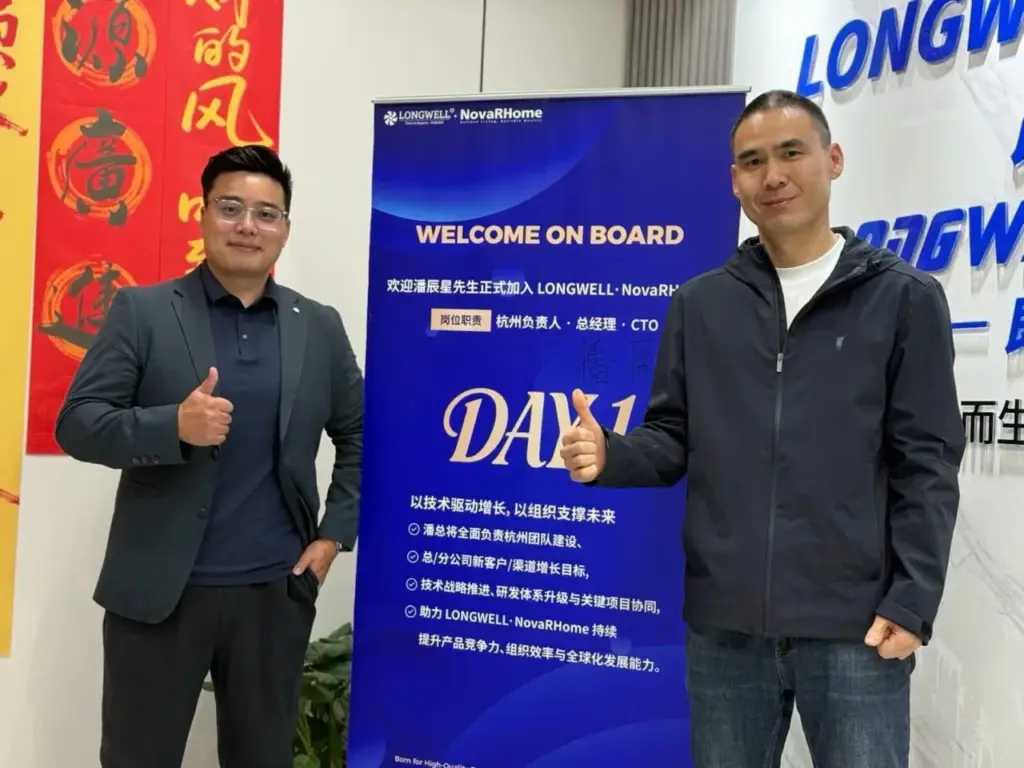 两位男士站在蓝色 WELCOME ON BOARD 欢迎展架两侧，面向镜头竖起拇指