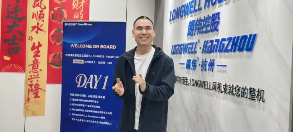一名身穿深色外套的男士站在 LONGWELL HANGZHOU 品牌墙与欢迎展架之间微笑鼓掌